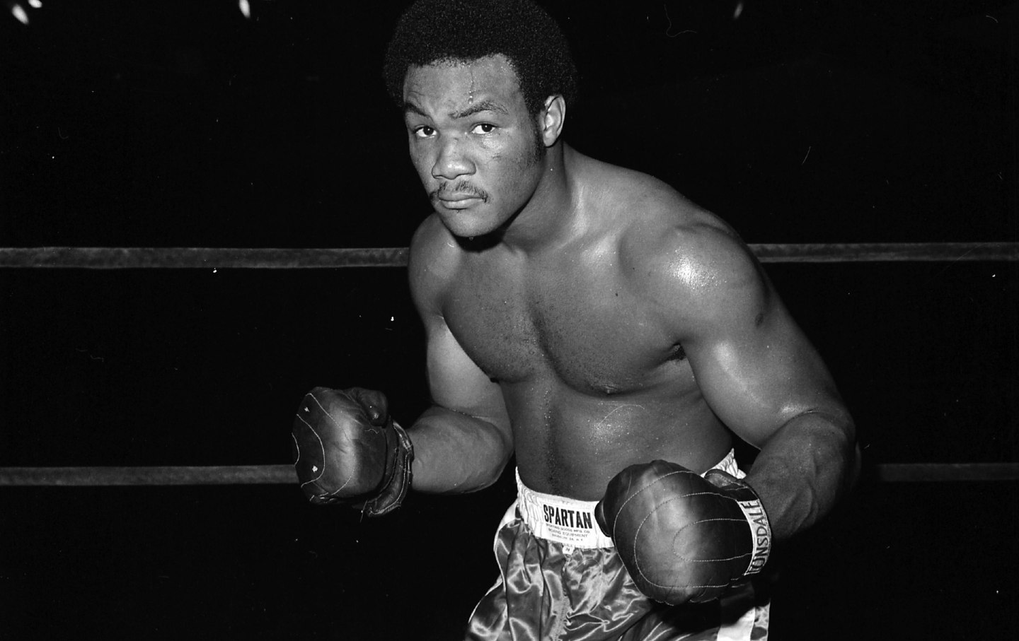 George Foreman smiling with belts, among the 10 Most Famous Boxers in the World for his comeback and knockout power.